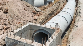 Cranes operate at a construction site during sunset, with workers actively engaged in building activities on the structure.