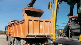 Cranes operate at a construction site during sunset, with workers actively engaged in building activities on the structure.