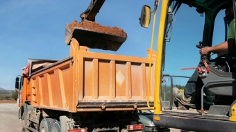 Cranes operate at a construction site during sunset, with workers actively engaged in building activities on the structure.