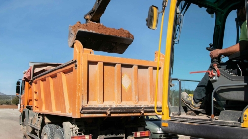 Cranes operate at a construction site during sunset, with workers actively engaged in building activities on the structure.