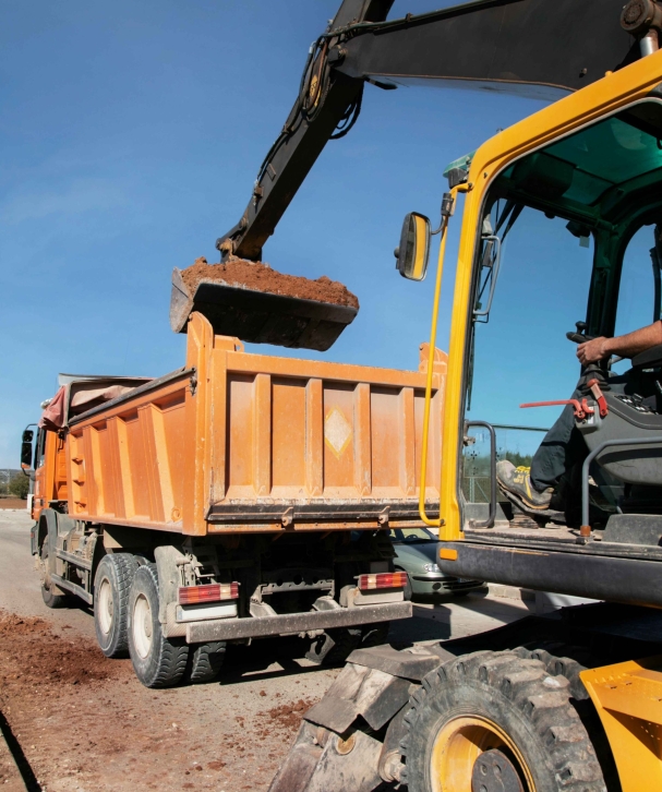 Cranes operate at a construction site during sunset, with workers actively engaged in building activities on the structure.