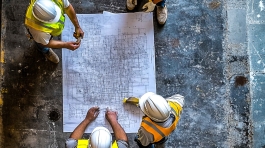 Cranes operate at a construction site during sunset, with workers actively engaged in building activities on the structure.