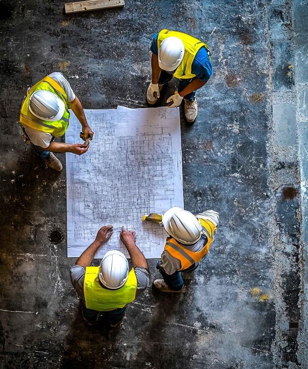 Cranes operate at a construction site during sunset, with workers actively engaged in building activities on the structure.