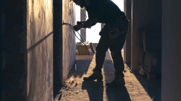Cranes operate at a construction site during sunset, with workers actively engaged in building activities on the structure.