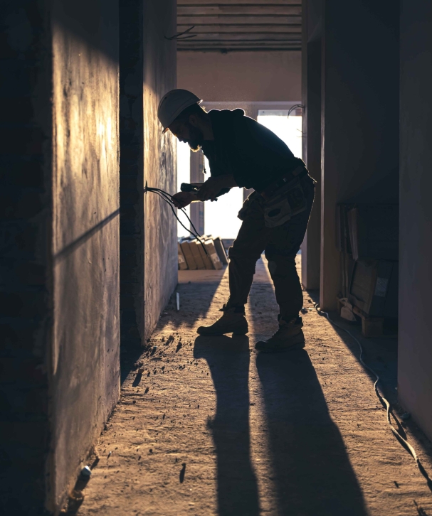 Cranes operate at a construction site during sunset, with workers actively engaged in building activities on the structure.